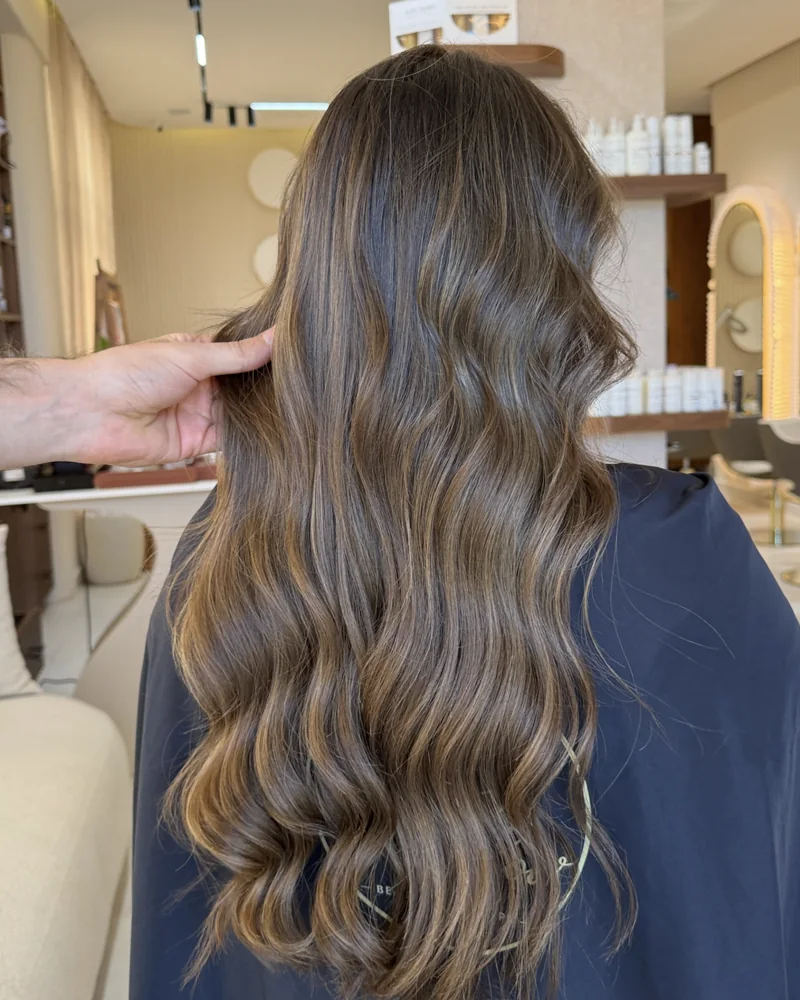 Balayage sur cheveux longs ondulés, vus de dos dans le salon