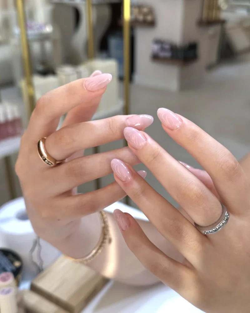 Ongles nude effet naturel, mains baguées devant les étagères du salon