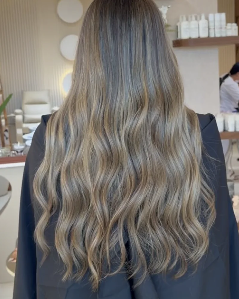 Balayage blond sur cheveux longs ondulés, vus de dos dans le salon