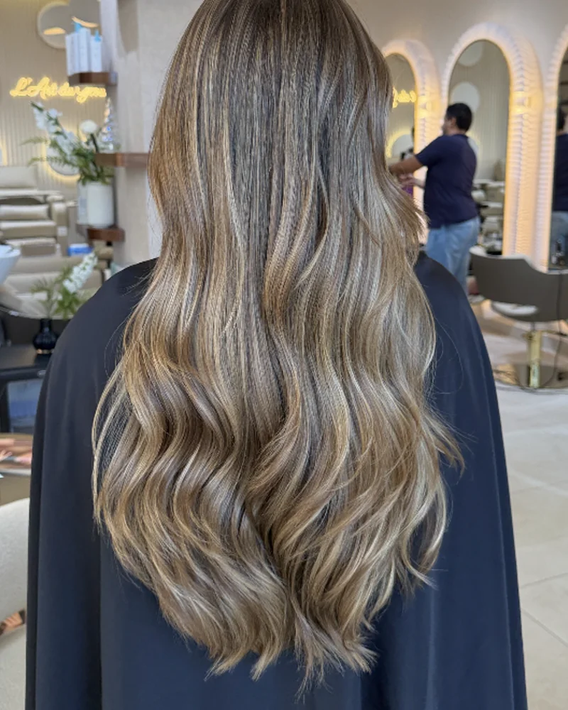 Cheveux longs ondulés après un brushing, vus de dos devant les étagères du salon
