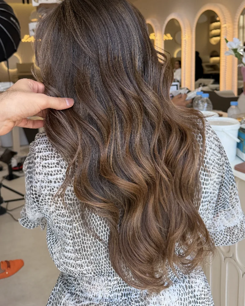 Ombré châtain sur cheveux longs ondulés, vus de dos dans le salon
